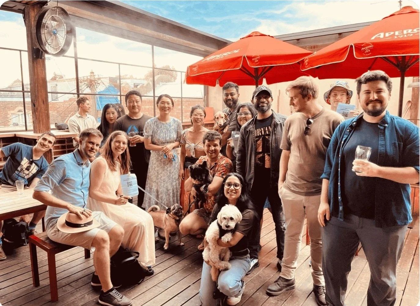 Pawshare Club members and their dogs gathered on a cafe terrace beneath red umbrellas