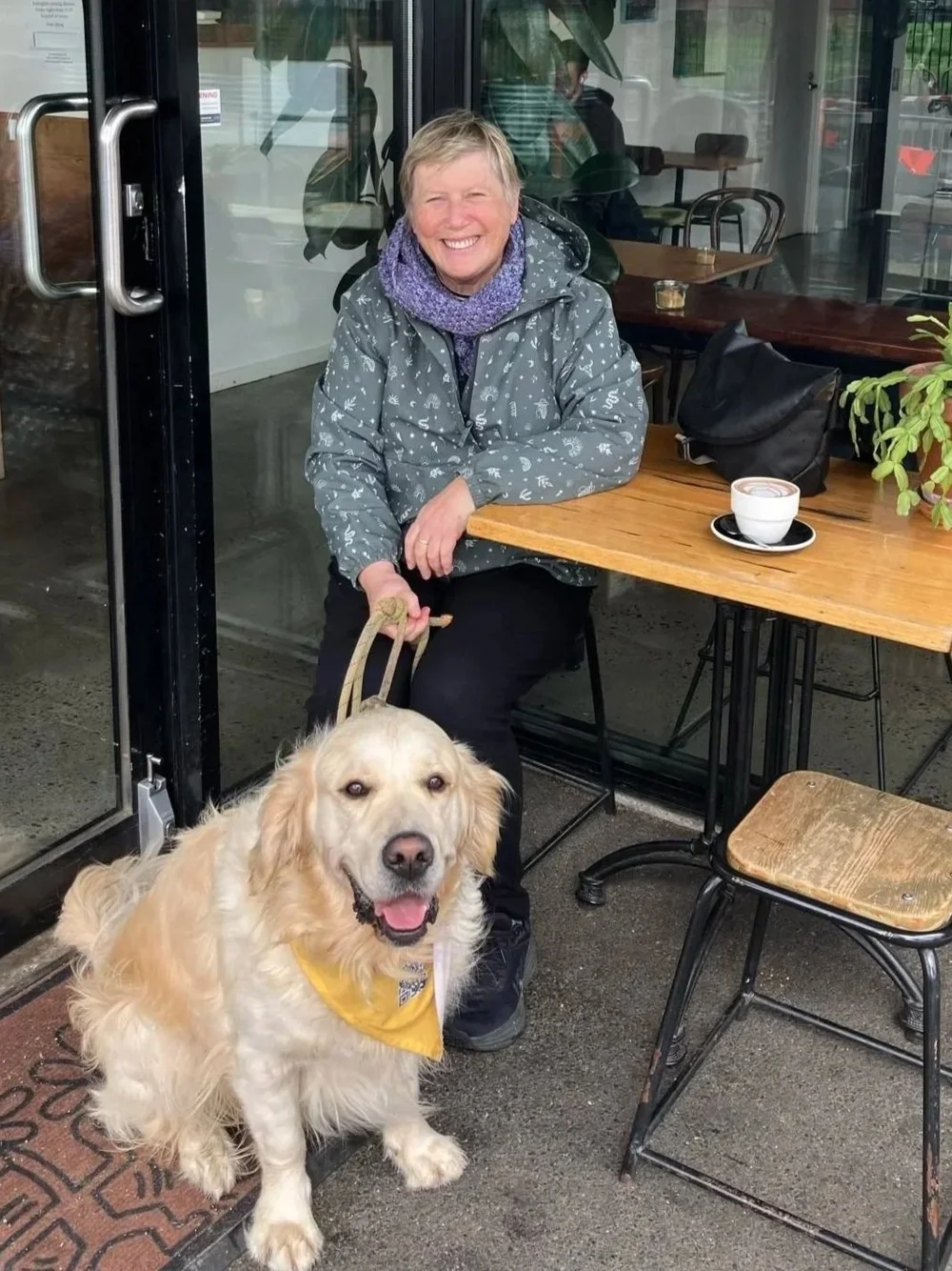 A person seated at an outdoor cafe table with a golden dog