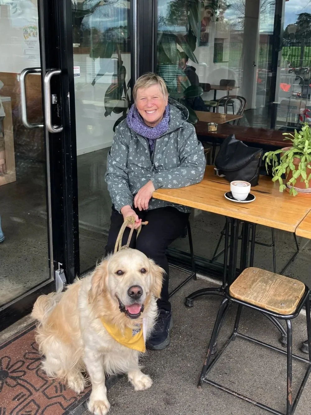 A person seated at an outdoor cafe table with a golden dog